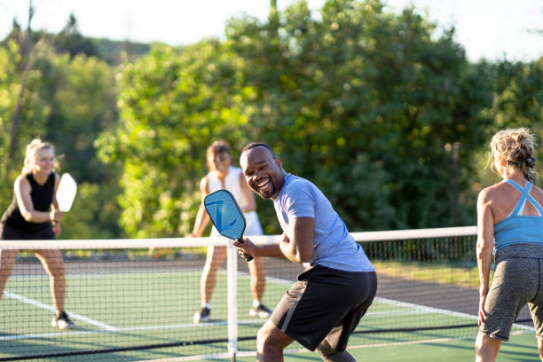 Playing pickleball A group of adults have fun while pickleball together on an outdoor court. pickleball stock pictures, royalty-free photos & images