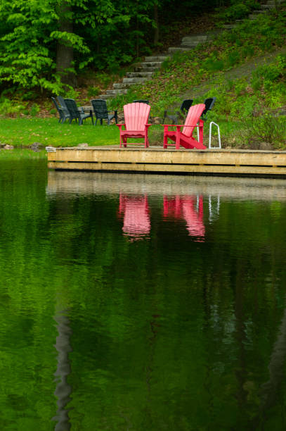 Two red Adirondack chairs on a cottage wooden dock reflecting on the calm waters of a lake in Muskoka.