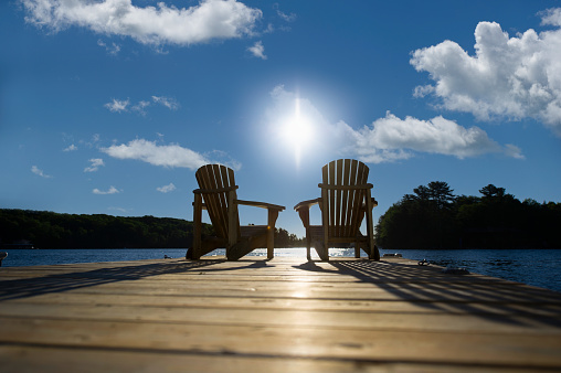 Cottage life - Sunrise on two empty Adirondack chairs sitting on a wooden pier on a lake in Muskoka, Ontario Canada.