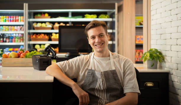 Portrait of a caucasian man working on cashier in a supermarket or retail shop, snacks and food on grocery products shelves. Food shopping. People lifestyle. Checkout business counter service. Worker stock photo
