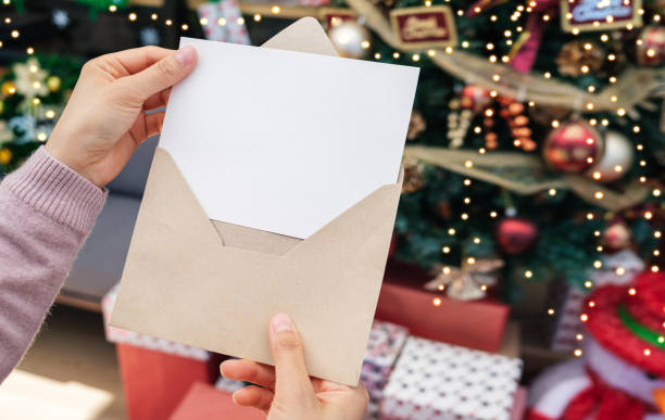 istock Woman's hand holding empty greeting card on background of christmas tree, gift box and ornaments. Merry christmas and happy new year concept 1434301227