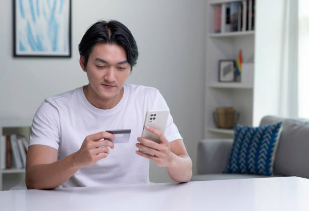 istock Young Asian man holding credit card and using smartphone. 1434308551