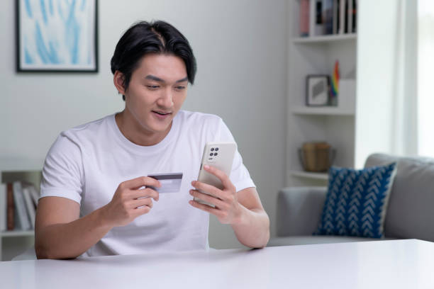 istock Young Asian man holding credit card and using smartphone. 1434308560