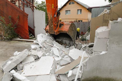 Demolition of old house. Excavator breaks building. City development, construction of new housing on site of old.