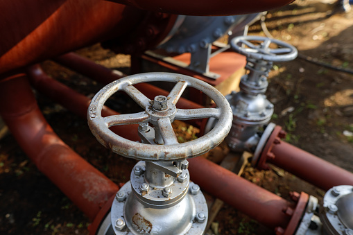 Shallow depth of field (selective focus) details with industrial metallic pipe valves used to open or close the hot water debit inside a big pipeline.