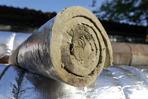 Shallow depth of field (selective focus) details with industrial glass wool used to thermal insulate a hot water metallic pipeline.