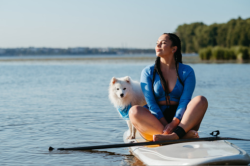 Young Woman Relaxing on the City Lake While Sitting on Sup Board with Her Dog Japanese Spitz