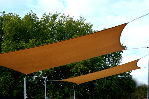 square canvas stretched, shading from sun and rain over terrace ofrestaurant, on playground in kindergarten, on platform of the promenade. pergola with metallic gray beams , cable, electric, bulb, led, tarp, grill, relax, place,  shadow,  rope, tense