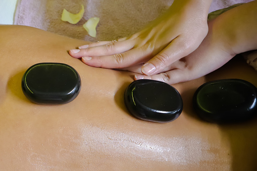 Stone-therapy massage close-up, hot stone treatment in beauty salon, hands and stones