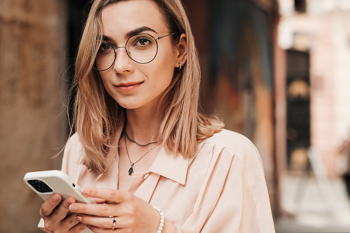 Close Up Portrait of Confident Young Woman with Eyeglasses Texting on Smartphone While Walking in the City, Blonde Girl in Glasses Using Mobile Phone