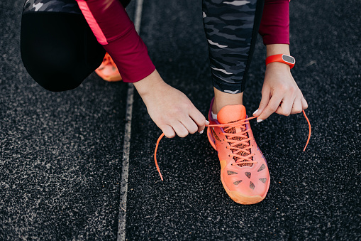 Unrecognisable woman tying laces on sports shoes for running on the running track at stadium