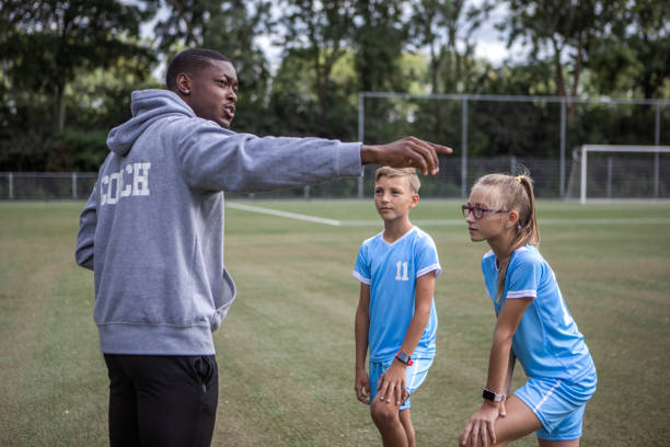 Handsome black soccer coach on a football pitch with two children stock photo