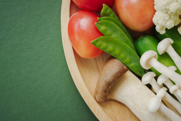 top view flat lay mix fresh vegetable with chinese cabbage,mushroom,tomato,green peas,cucumber with copy space on wood round plate dark green background.idea for vegan healthy food.