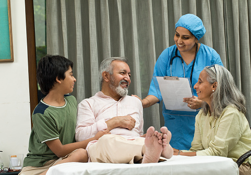 Female nurse and family with senior patient sitting on bed