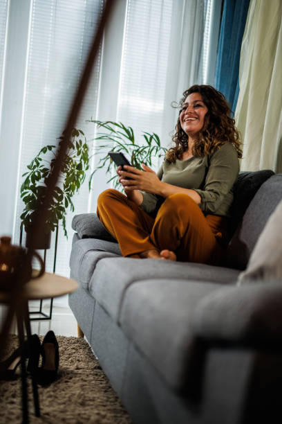 istock Contented woman lounging on the couch and using smart phone for fun 1434351414
