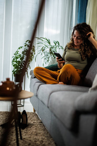 istock Contented woman lounging on the couch and using smart phone for fun 1434351426
