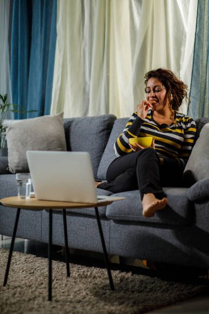 femme assise sur le canapé, grignotant des frites et regardant une émission de télévision - computer chip photos et images de collection