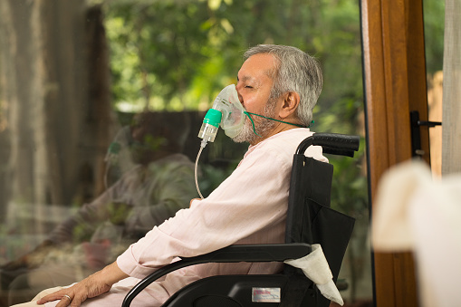 Senior man with oxygen mask sitting on wheelchair at home