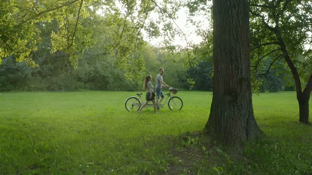 A couple on a tandem bike rides through the park between the trees
