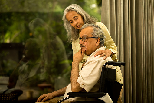 Loving woman consoling depressed old husband on wheelchair