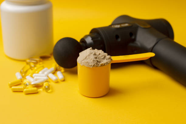 Therapeutic percussive massage gun, fit meal, pills, sport energy bar, protein on yellow background - concept of modern sport activity and diet, health lifestyle routine, wellness, healthcare pistola de masaje de percusión terapéutica, comida en forma, píldoras, barra energética deportiva, proteína sobre fondo amarillo: concepto de actividad deportiva moderna y dieta, rutina de estilo de vida saludable, bienestar, atención médica