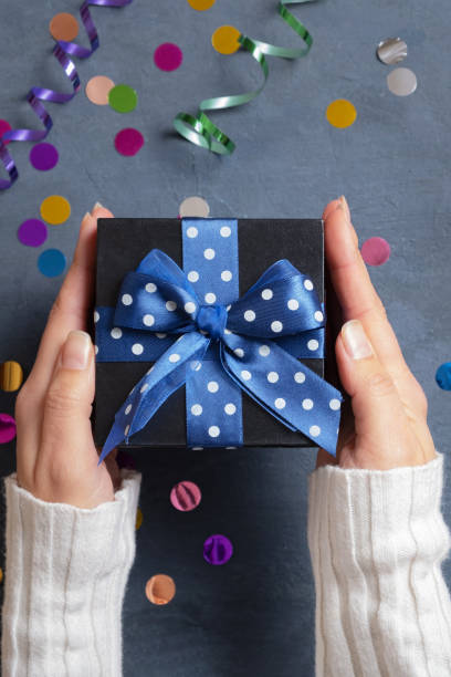 istock Female hands with a gift and festive tinsel flat lay on a dark cement background. Vertical photo 1434357069