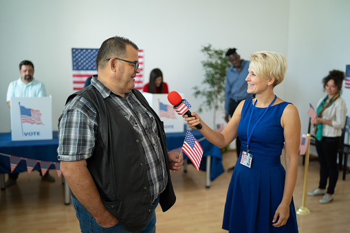 Young female reporter taking interview from a man at election voting center