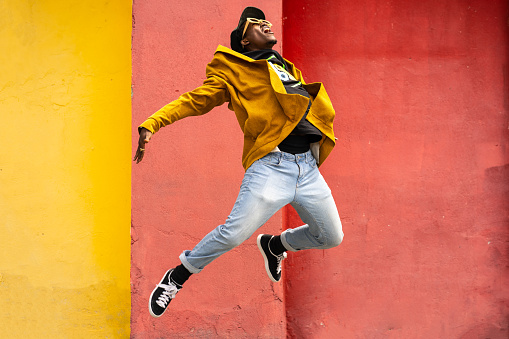 Young African-American man is mid pose in the air with arms and legs kinked backwards, wearing modern clothing against orange and yellow background