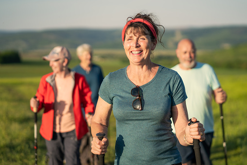 A retired woman is happily leading a walking group across the beautiful green and grassy countryside