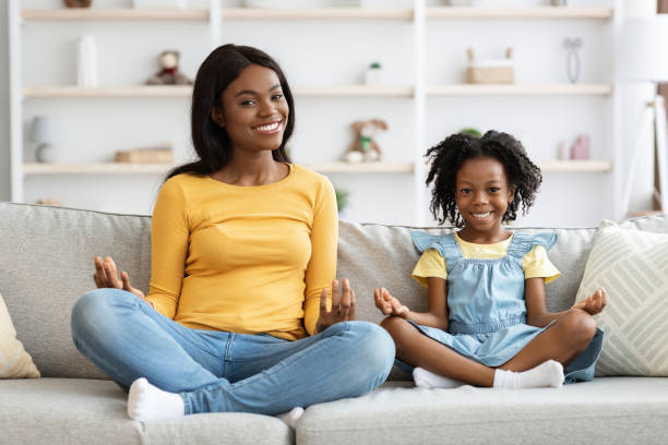 garota negra alegre e sua mãe sentada no sofá em posion lotus - posion - fotografias e filmes do acervo