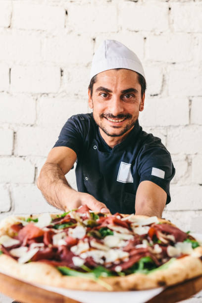 istock Smiling Italian chef pizzaiolo offering pizza in restaurant 1434363402