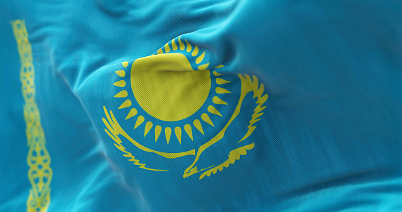 Close-up view of the Kazakhstan national flag waving in the wind. The Republic of Kazakhstan is a transcontinental state straddling Asia and Europe. Fabric textured background. Selective focus