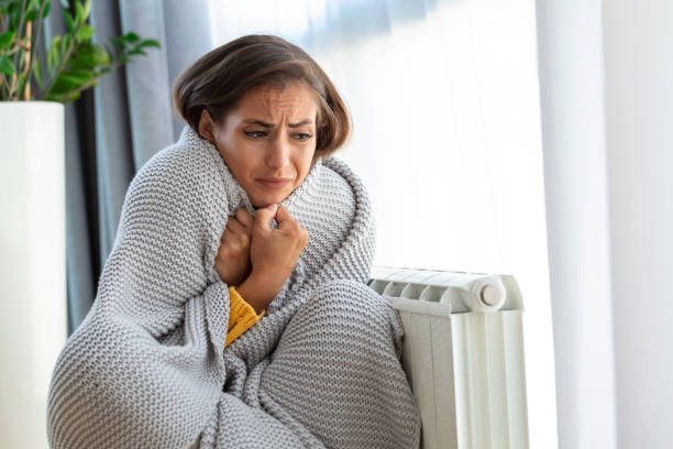 Unwell woman renter in blanket sit in cold living room hand on old radiator.suffer from lack of heat . Unhealthy young woman struggle from chill freeze at home. No heating concept. Unwell woman renter in blanket sit in cold living room hand on old radiator.suffer from lack of heat . Unhealthy young woman struggle from chill freeze at home. No heating concept. space heater stock pictures, royalty-free photos & images