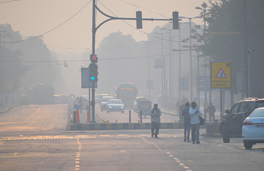 Delhi, India - November 21, 2017: Daily commuters walk along a road amidst heavy smog conditions in New Delhi.