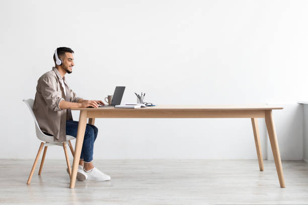 istock Smiling Arab man in headphones using pc at home 1434368715