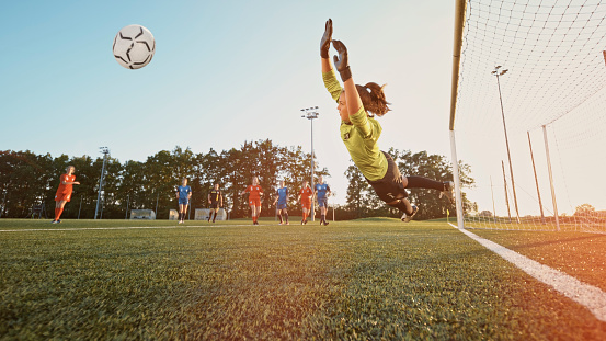 Female football player goalkeeper jumping to catch football during match.