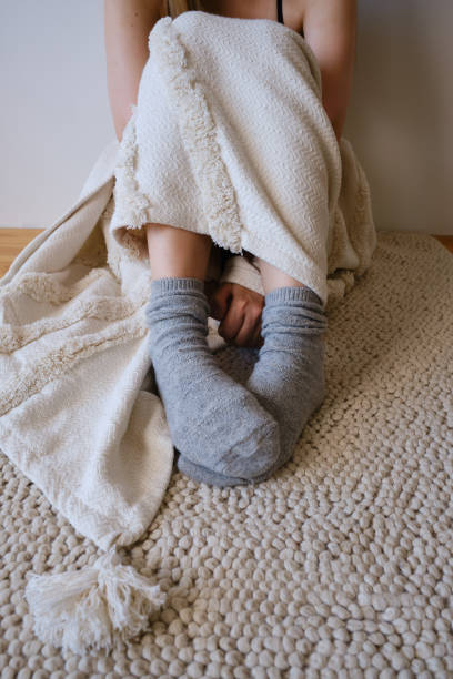 The woman lies in warm gray socks in bed and covers herself with a blanket. Women's legs in cozy socks. View from above. Warm evenings at home stock photo