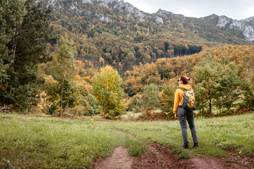 Mid adult woman carrying a backpack, hiking alone in mountains in autumn, enjoying beautiful nature.