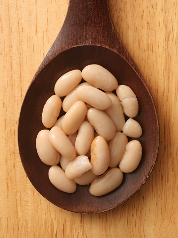 Top view of wooden spoon over table with soaked cannellini beans on it