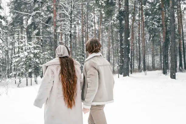 Love romantic young couple girl, guy in snowy winter forest with christmas tree. Walking, having fun, laughing in stylish clothes, fur coat,jacket, woolen shawl. Snow lovestory. Romantic date,weekend.