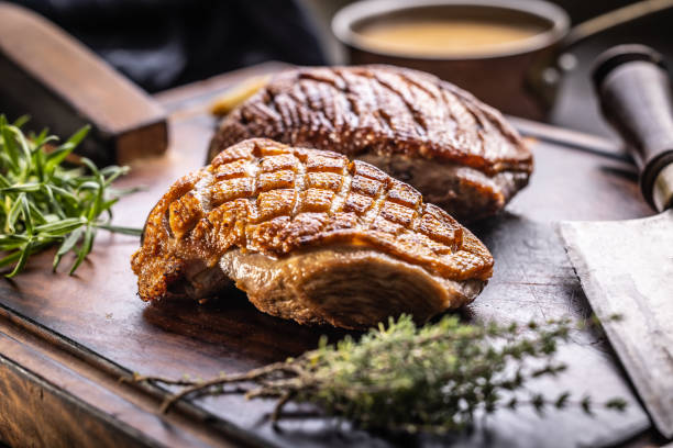 Roasted duck breast on a cutting board with rosemary and thyme herbs.
