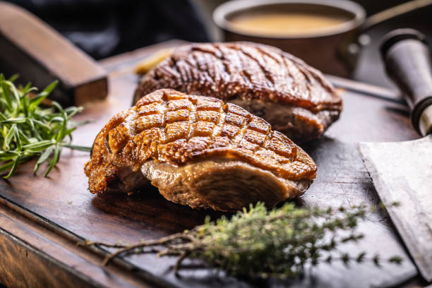 Roasted duck breast on a cutting board with rosemary and thyme herbs. stock photo