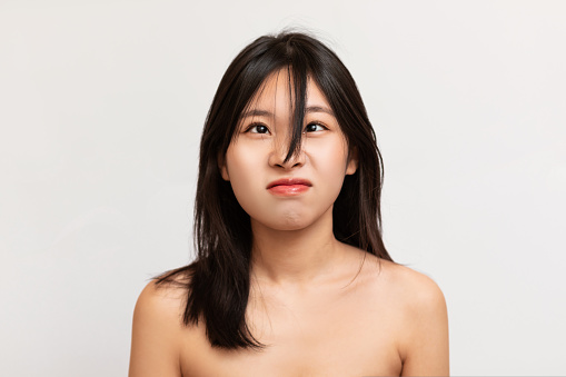 Portrait Of Angry Young Asian Woman Looking Up At Her Bangs Hair, Unhappy Beautiful Lady Wants To Cut Her Fringe And Going For A New Look And Hairstyle Isolated Over White Studio Background Wall