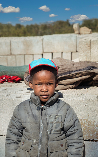 Village kid standing in front of a pile of bricks, village in botswana