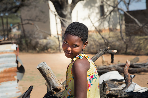 African girl with yellow dress sited in the yard on a wood pile