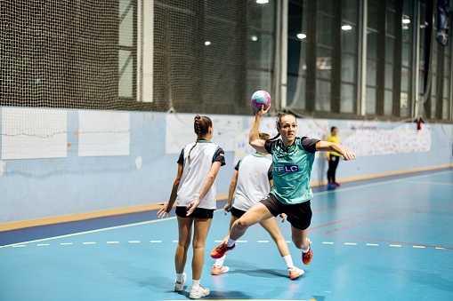 Woman volleyball player jumping high and kicking ball through net during sports training in dark indoors stadium back view