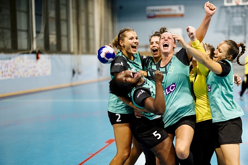 Group of multi-ethnic female handball players celebrating huddled in circle after winning match