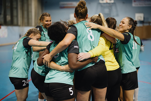 Group of multi-ethnic female handball players celebrating huddled in circle after winning match