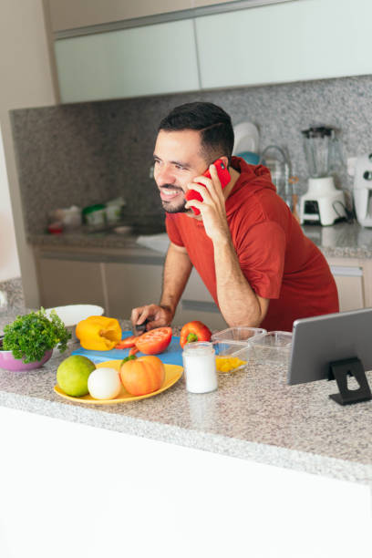 istock Young Man talking on cell phone while preparing breakfast at home 1434392097