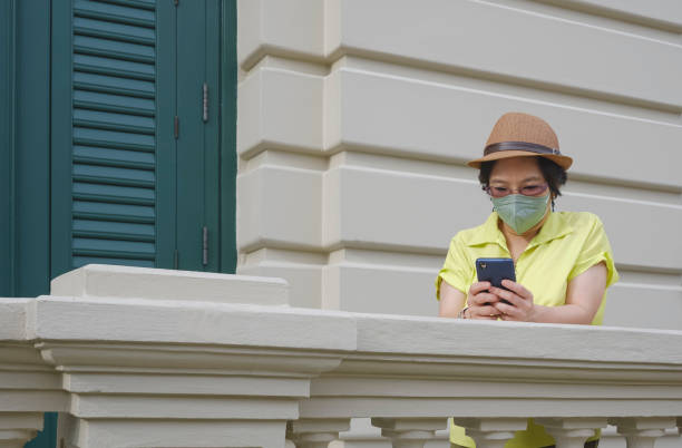 istock Asian female tourist in vintage style and protective face mask using smartphone while standing on terrace of historical building 1434392389